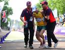 El marchador australiano Nathan Deakes (C) ayudado por voluntarios tras cruzar la l&iacute;nea de meta de los 50 km marcha.