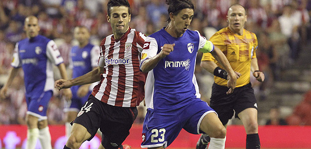 El capit&aacute;n del Hapoel Kiryat Shmona FC, Adrian Rochet disputa un bal&oacute;n con el delantero del Athletic Club de Bilbao Markel Susaeta.