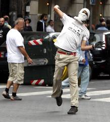 Un encapuchado lanza a una piedra a agentes de la brigada m&oacute;vil de la Ertzaintza que ha detenido al menos tres personas en los altercados que se han producido este mediod&iacute;a en el centro de la capital vizca&iacute;na.