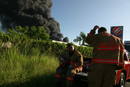Bomberos descansan mientras se levanta una columna de humo debido al incendio de varios tanques de la refiner&iacute;a de petr&oacute;leo de la empresa Caribbean Petroleum Corporation.