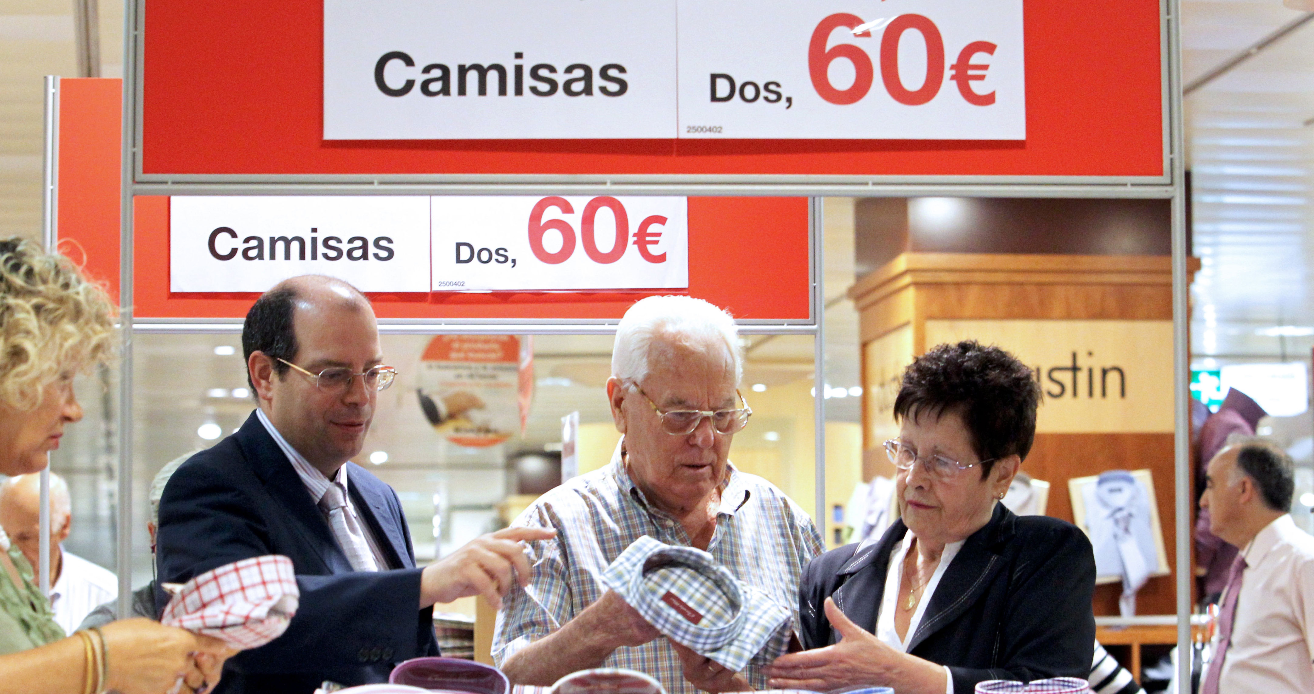 Un empleado de un centro comercial de Bilbao atiende a un matrimonio en la secci&oacute;n de camiser&iacute;a en el primer d&iacute;a de rebajas.