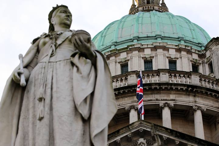 Una estatua de la reina Victoria aparece en primer plano frente al ayuntamiento de Belfast, donde ondea la Union Jack, la bandera brit&aacute;nica