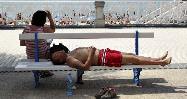 Dos personas descansan a la sombra en el paseo de la playa de La Concha de San Sebasti&aacute;n.