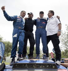 Sainz celebra la victoria con su copiloto Lucas Cruz y dos miembros del equipo Volkswagen sobre el cap&oacute; de su Tuareg.
