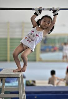 Una niña del equipo de gimnasia infantil de Nanjing, China, con las manos atadas en la barra horizontal, preparándose para su entrenamiento deportivo. Una niña del equipo de gimnasia infantil de Nanjing, China, con las manos atadas en la barra horizontal, preparándose para su entrenamiento deportivo.