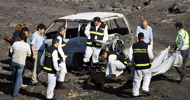 Forensics inspect the blackened corpse of a fire-fighter after deadly forest fire in central Spain.