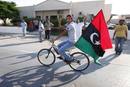 Un j&oacute;ven lleva en un bicicleta la nueva bandera del Reino de Libia por las calles de Janzour