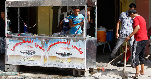 Jóvenes recogen los cristales rotos de su establecimiento tras la explosión de un coche bomba en Bagdad.