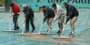 Los encargados del mantenimiento de las pistas de tenis quitan el agua de las cubiertas de lluvias tras un chaparr&oacute;n.