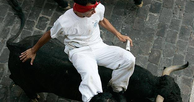 Un mozo a lomos de un toro en uno de los encierros de San Ferm&iacute;n