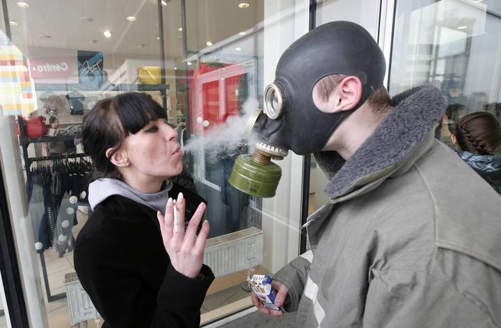 Una mujer lanza humo sobre un activista que lleva una m&aacute;scara antig&aacute;s e nun protesta anti tabaco en Rusia.