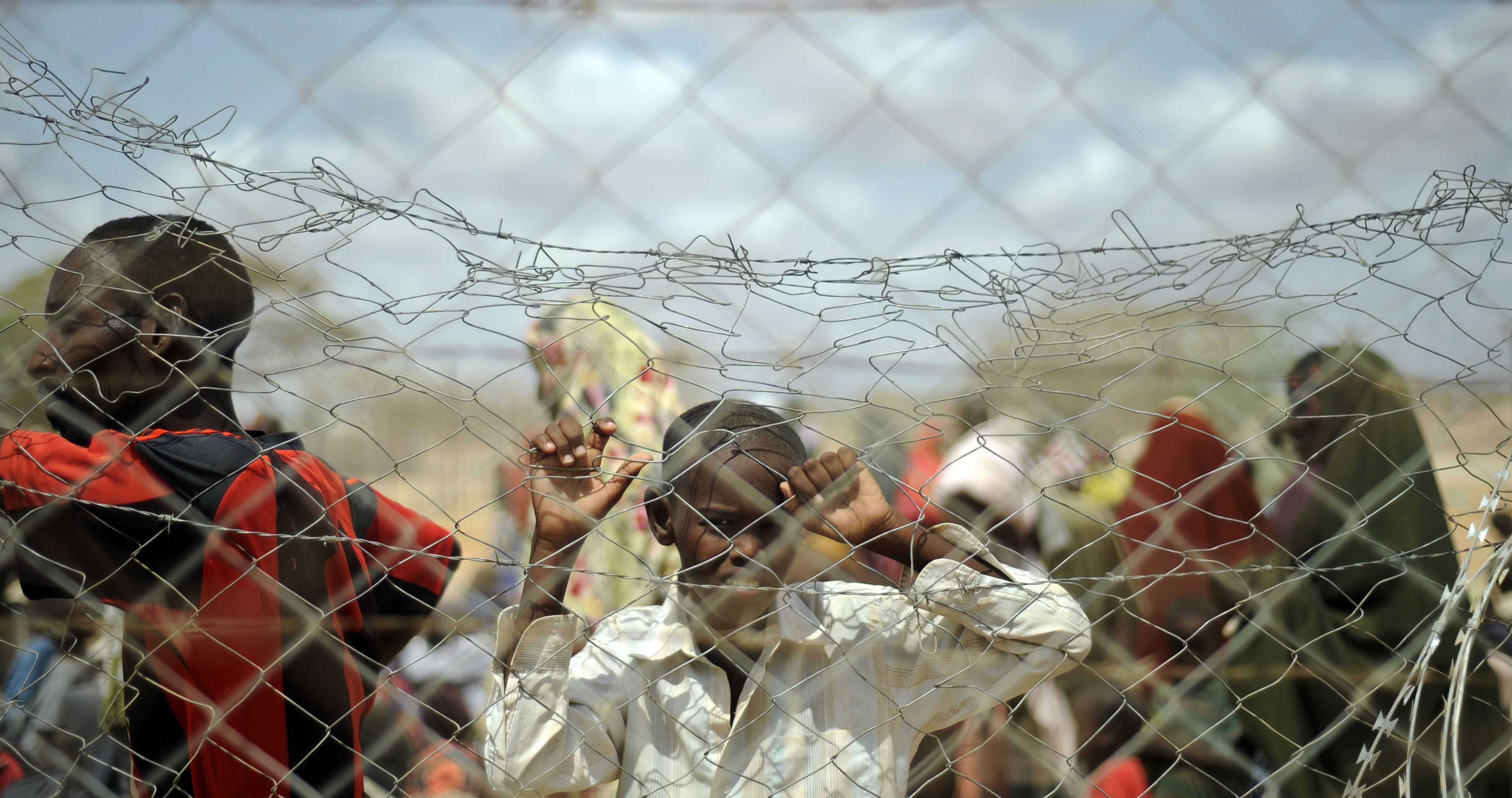 Un niño mira a través de una valla cómo llegan refugiados al campamento de Al Dadaab, en Kenia. Un niño mira a través de una valla cómo llegan refugiados al campamento de Al Dadaab, en Kenia.