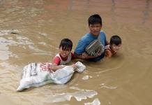 Un padre ayuda a sus hijos a cruzar una calle completamente inundada, en la poblaci&oacute;n de Santa Cruz, en la provincia de Laguna, al sur de Manila (Filipinas),