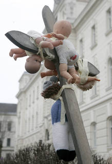 A children's rights activist holds up a cross with dolls attatched in front of the courthouse in St. Poelten