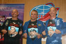 Los tres tripulantes muestran sus camisetas con dibujos durante la rueda de prensa en el cosm&oacute;dromo de Baikonour.