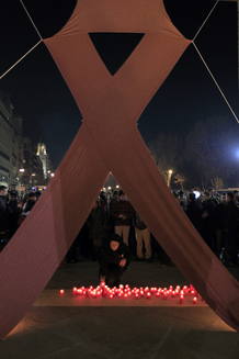 Una mujer enciede una vela en un acto en memoria de los fallecidos en España victimas del Sida en el que se colocó un gran lazo rojo en la puerta de Alcalá Una mujer enciede una vela en un acto en memoria de los fallecidos en España victimas del Sida en el que se colocó un gran lazo rojo en la puerta de Alcalá