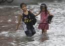 Dos ni&ntilde;os caminan por las calles inundadas de malob&oacute;n, al norte de Manila
